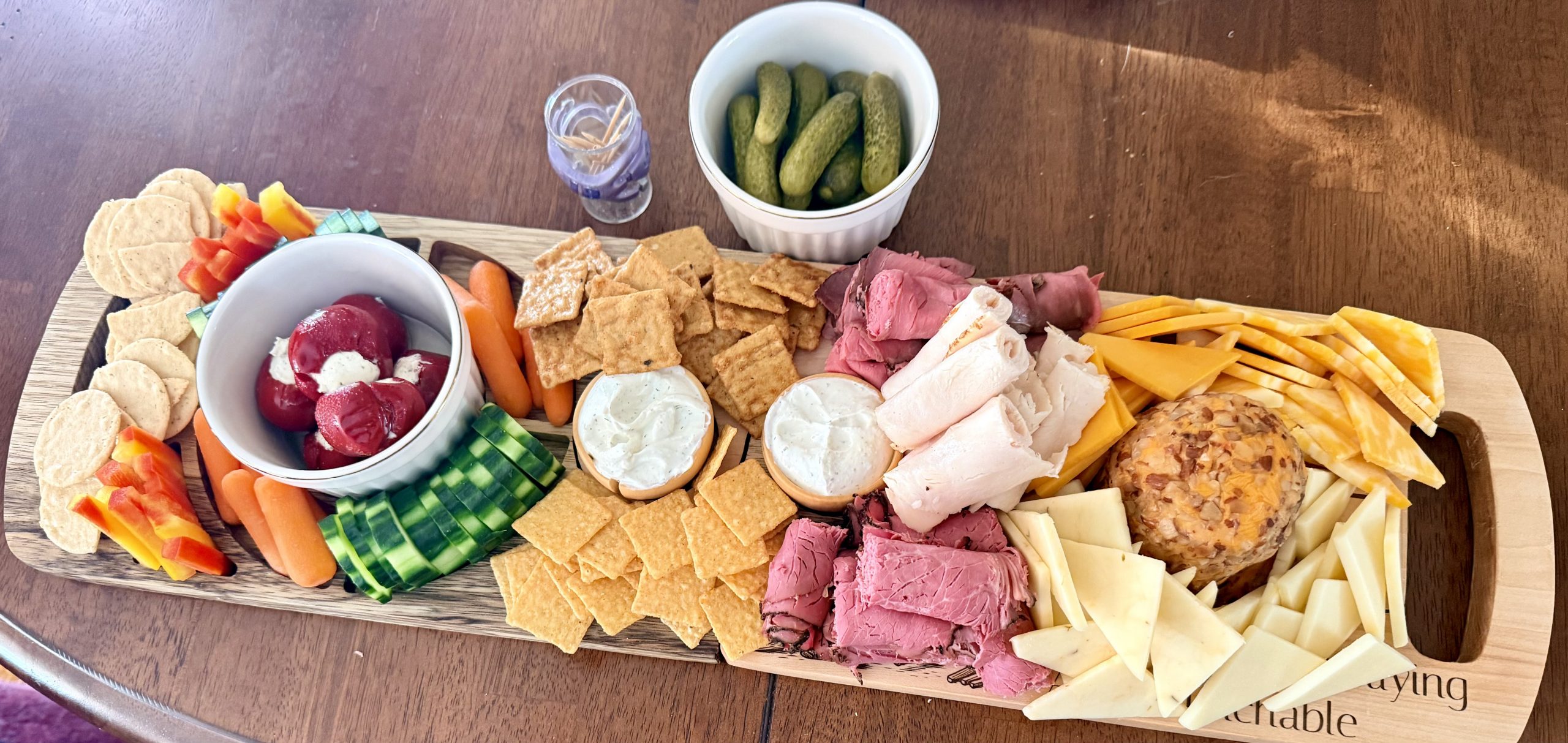 Handcrafted hardwood charcuterie board arranged with cheeses, meats, crackers, and vegetables