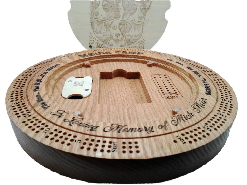 Round cedar cribbage board with engraved memorial text, peg track scoring, recessed storage compartments, and magnetic lid closure.