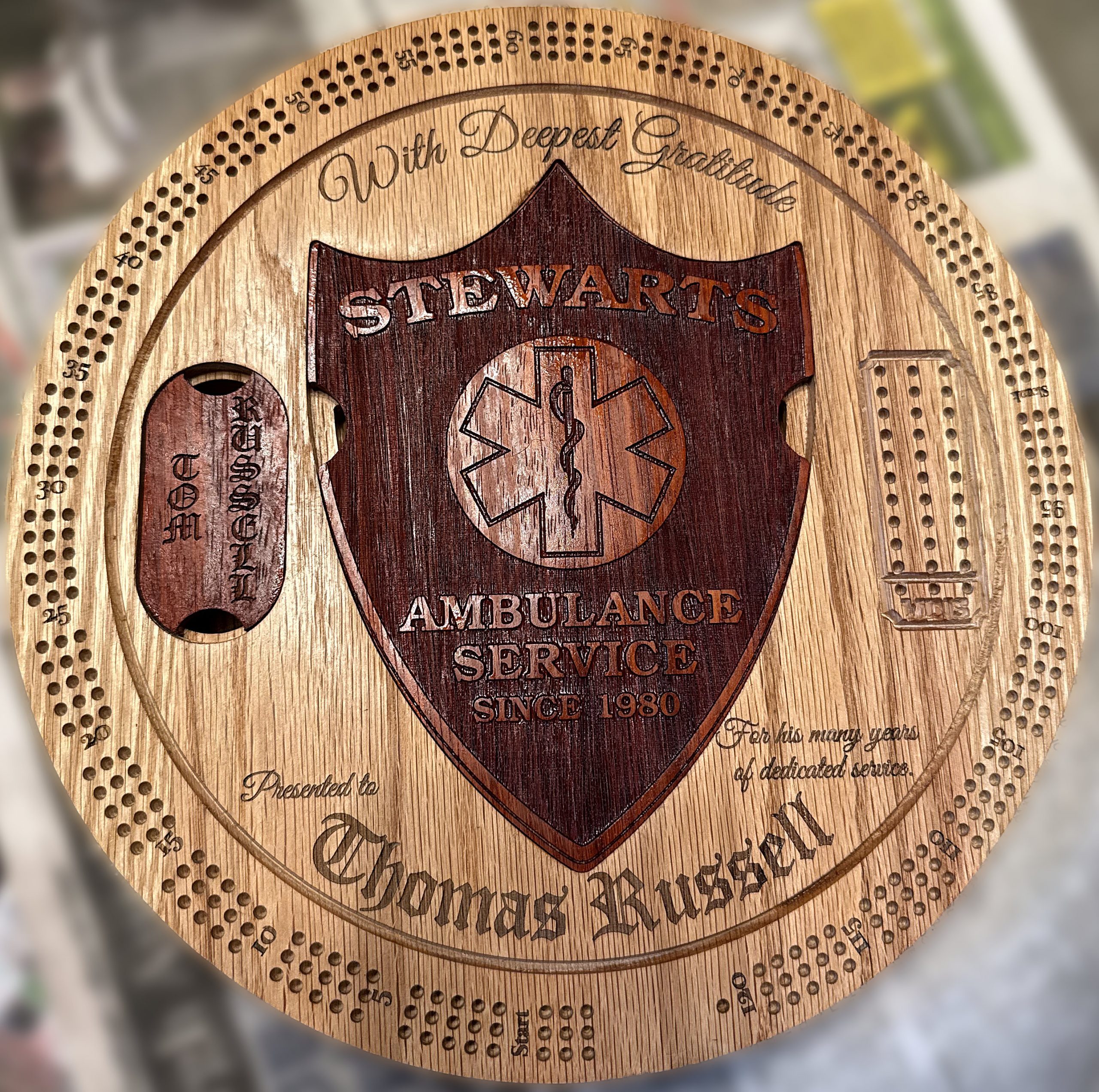 Tom Russell retirement cribbage board with red oak construction, Padauk shield, engraving, and integrated storage